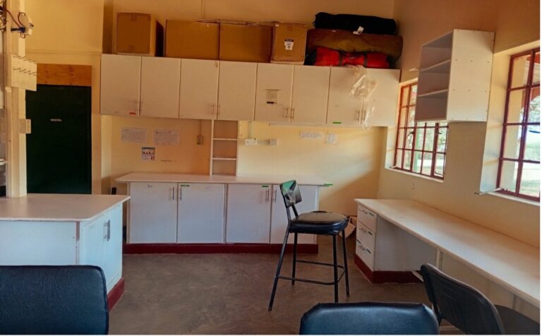 Wet lab with white benches, wall cabinets and stools beside a doorway